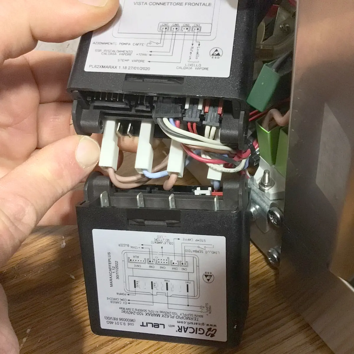 A close-up of a person’s hand connecting wiring inside an espresso machine, with labeled circuit components and various colored wires visible—potentially working on the Brain Unit of a Lelit Mara X.