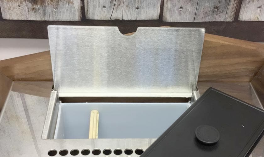 A close-up of a metal chafing dish with its lid partially open reveals a white insert and wooden stir stick, echoing the warm, refined ambiance typical of settings featuring the Nurri L-Type Lever Dual Boiler Espresso Machine. © 2025 1st-line.com