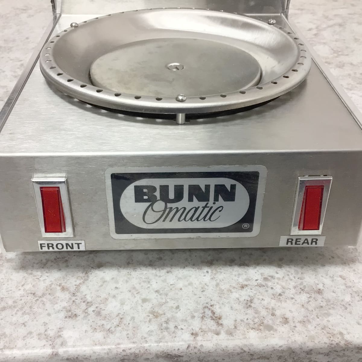 A close-up of the SIDEWALK SALE - Bunn Dual Warmer (E109) shows two red switches labeled FRONT and REAR on a speckled countertop, its round metallic plate with a raised edge—ideal for keeping coffee warm at your next event. © 2025 1st-line.com