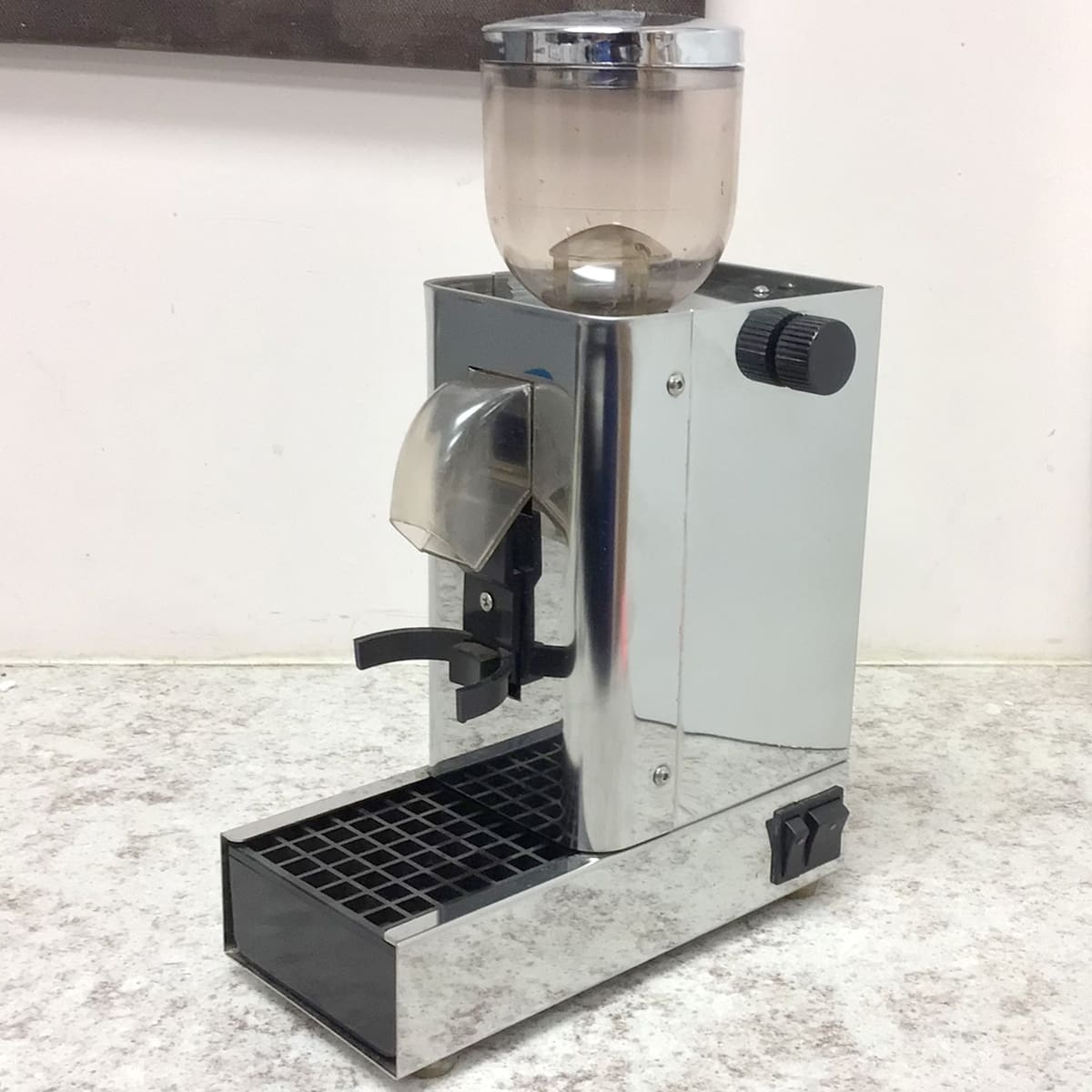 A SIDEWALK SALE - Test Conical Burr Espresso Grinder (E109) with a transparent bean hopper and black dial sits on a speckled countertop, featuring a portafilter holder and drip tray—ideal for espresso lovers. © 2025 1st-line.com