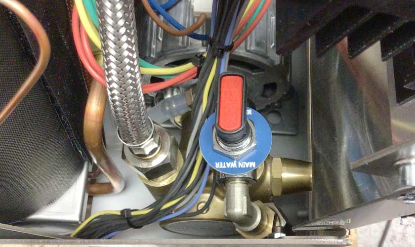 Close-up of internal plumbing and wiring in the Nurri L-Type Lever Leva Dual Boiler Espresso Machine, showcasing a red and black water valve, braided metal hose, colored wires, metal pipes, and dual boiler components. © 2025 1st-line.com
