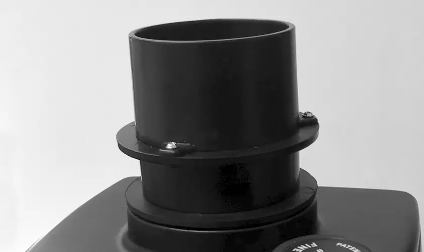 A close-up of a cylindrical black plastic pipe fitting with screws, mounted on a flat black surface against a plain background—resembling components in the Eureka Atom W 75 Weight Based Espresso Coffee Grinder. © 2025 1st-line.com