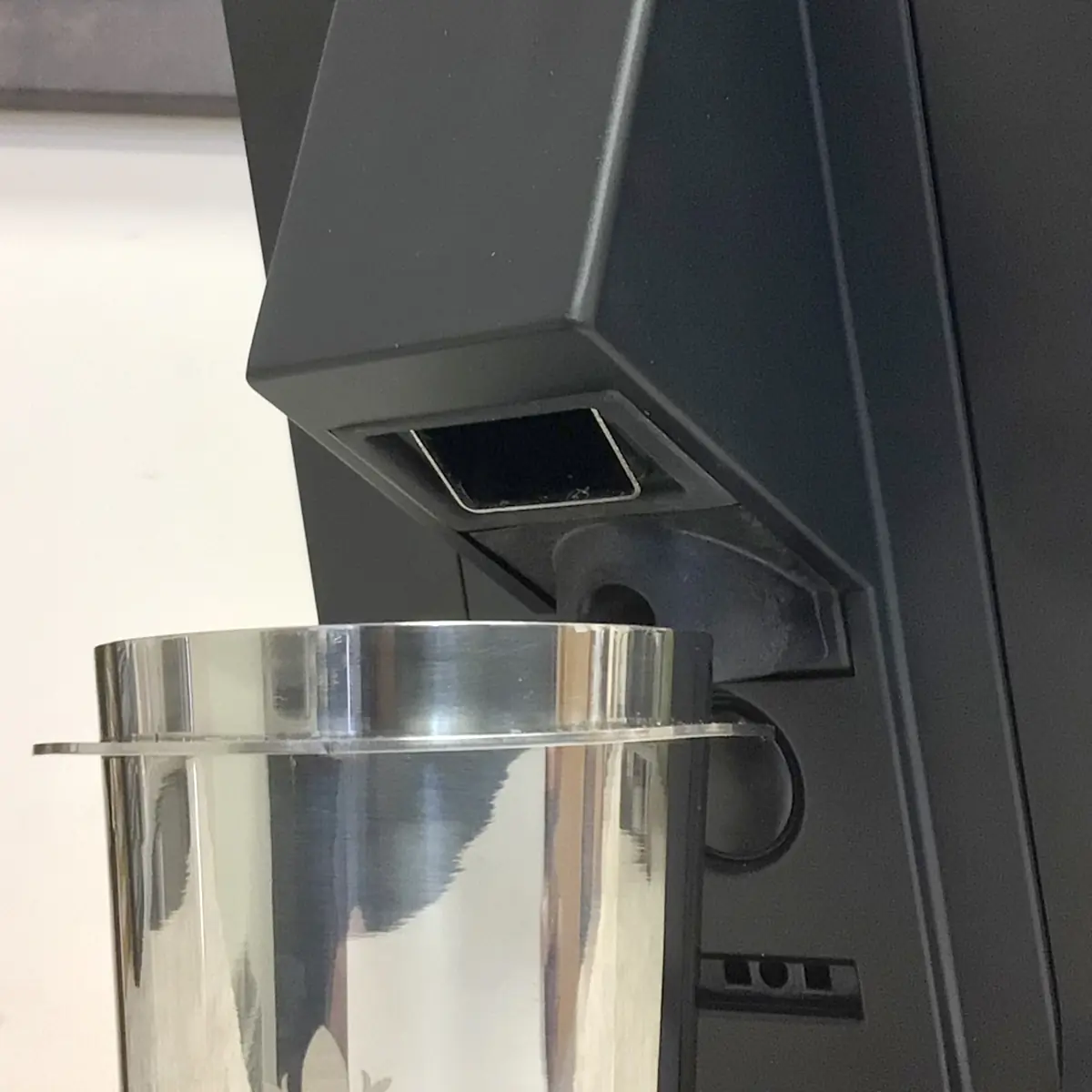 A close-up of a shiny metal cup under the dispenser of a black coffee machine, ready to be filled—ideal for pairing with the Eureka Mignon Single Dose Espresso Coffee Grinder.