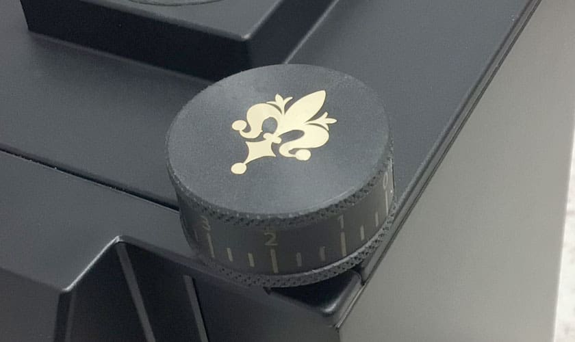 A close-up of a black combination lock with a gold fleur-de-lis on the dial, attached to a black safe, evokes the precision found in the Eureka Mignon Single Dose Espresso Coffee Grinder. © 2025 1st-line.com