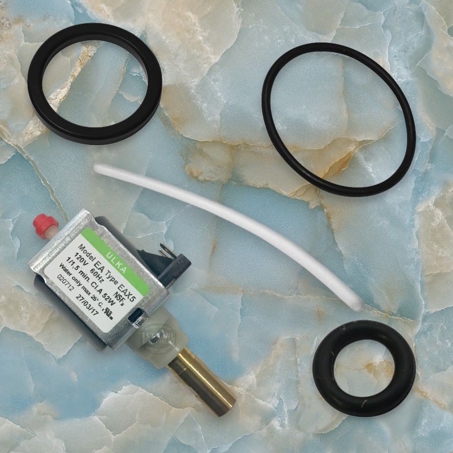A small solenoid valve with a label, two large black O-rings, one smaller O-ring, and a short white tube are arranged on a marble-patterned surface—ideal for an espresso machine with no plastic components. © 2025 1st-line.com
