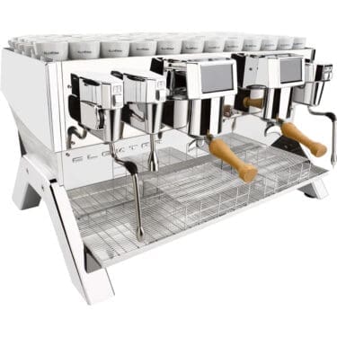 A spacious, modern Elektra Indie Smart 2GR espresso machine in white/stainless with dual group heads, dual steam wands, digital display, wooden handles, and stacked cups on top. Its sleek chrome finish runs on 220 volts. © 2025 1st-line.com