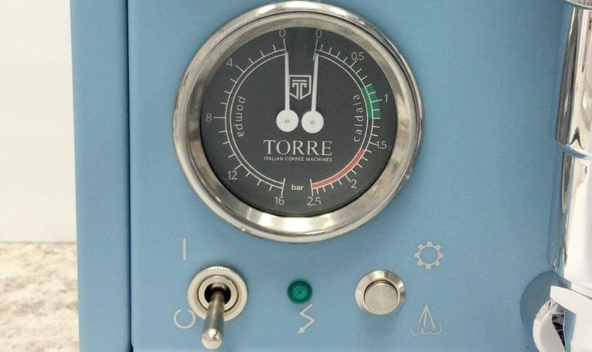 Close-up of a blue Torre Luigino HX Espresso Machine w/ Flow Control, showing a round TORRE-labeled pressure gauge with flow control, color markings, a metal switch, green indicator light, and various control symbols below the gauge. © 2025 1st-line.com