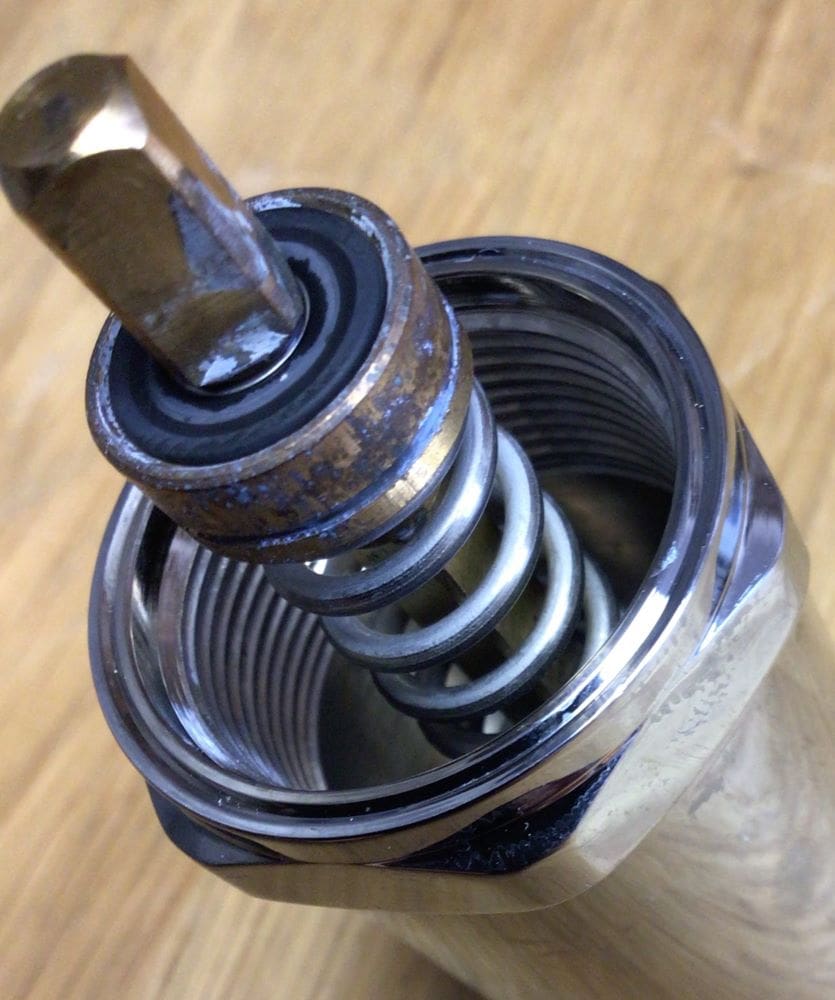 Close-up of a metal valve with a spring and threaded interior, showing some rust and wear, positioned on a wooden surface—similar to those found in Lelit Bianca machines that may experience a leak issue even when brand new. © 2025 1st-line.com