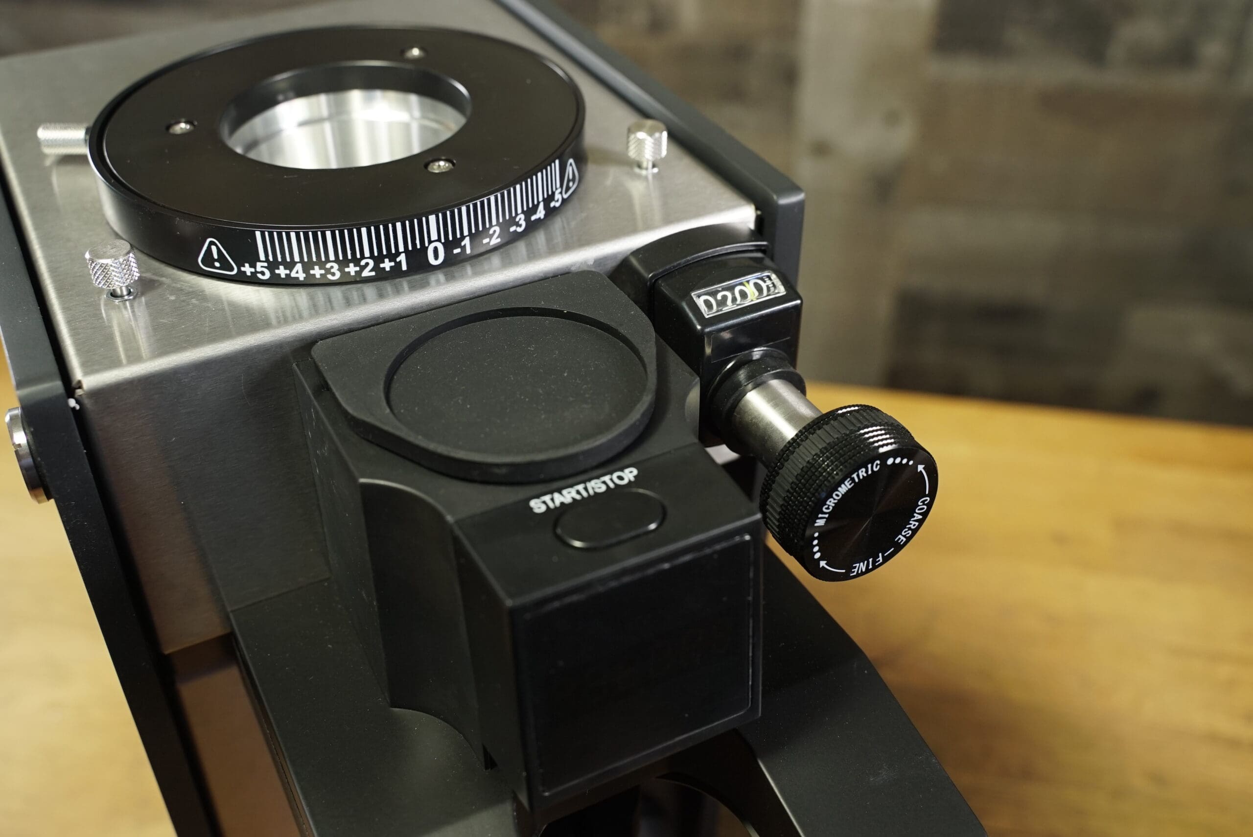 Close-up of the Slingshot Dosis S75 Espresso Coffee Grinder Black 220Vs adjustment dial, timer, black start/stop button, and textured knob with numbered grind settings against a blurred wood background. © 2025 1st-line.com