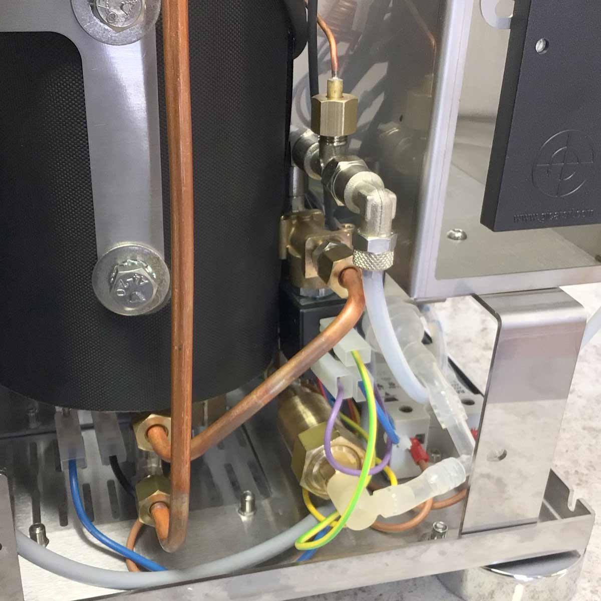 Close-up of the Torre Luigino HX Espresso Machine w/ Flow Control, highlighting copper pipes, metal parts, flow control devices, plastic tubes, and colorful electrical wires neatly arranged inside the metallic frame. © 2025 1st-line.com