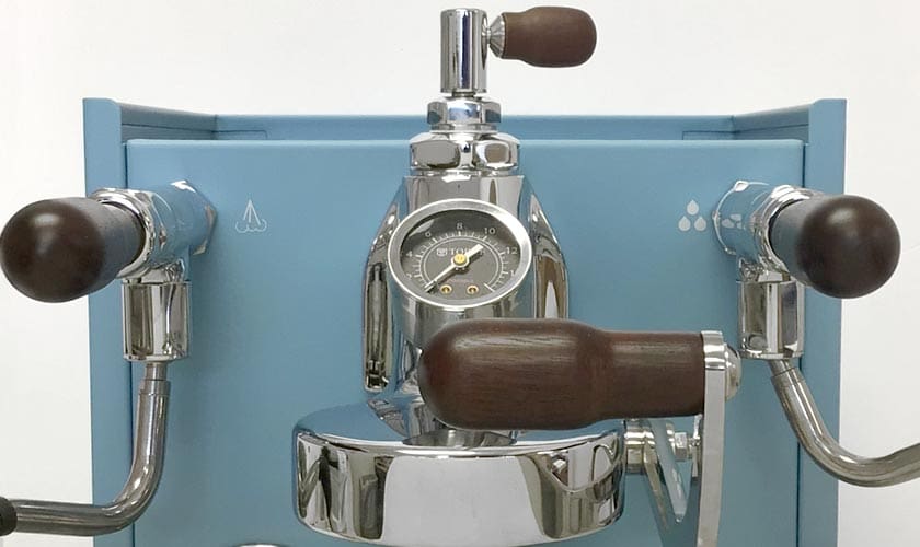 Close-up of the Torre Luigino HX Espresso Machine w/ Flow Control in blue, featuring chrome and dark wood handles, a central pressure gauge, and simple white water and steam symbols for easy flow control. © 2025 1st-line.com