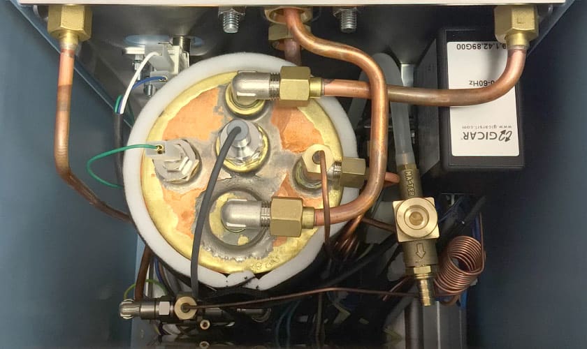 Close-up of the Torre Luigino TSP HX Espresso Machine w/ Flow Control reveals copper pipes, flow control parts, and a metal boiler with connectors. A ZIGGUR-branded box on the right highlights Torre Luigino craftsmanship. © 2025 1st-line.com