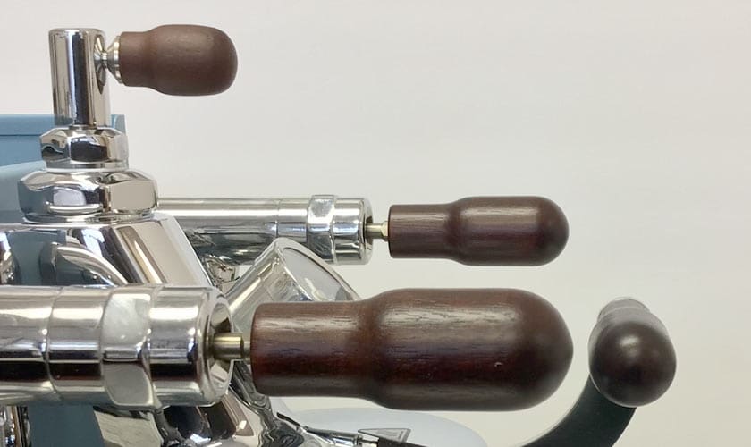 Close-up of three dark wooden levers and a black knob on the shiny Torre Luigino TSP HX Espresso Machine w/ Flow Control, showcasing its flow control features against a plain light background. © 2025 1st-line.com