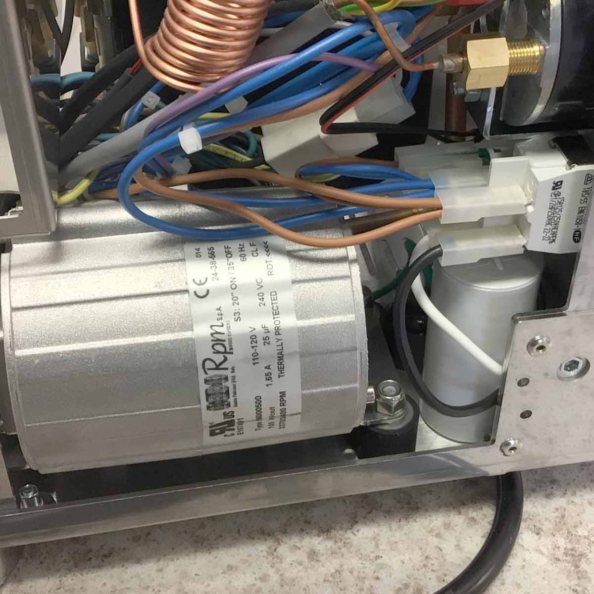 Close-up of Torre Luigino HX Espresso Machine w/ Flow Control’s internal components: visible electrical wiring, labeled silver motor, copper tubing, and flow control connectors are all mounted on a metal base. © 2025 1st-line.com