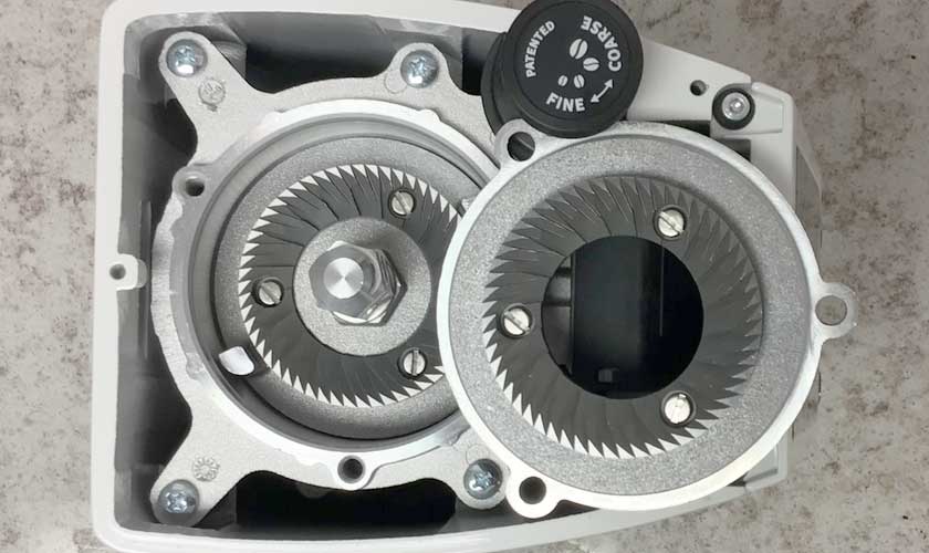 Top-down view of the Eureka Atom W 65 Weight Based Espresso Coffee Grinder, featuring two circular metal burrs with sharp teeth and an adjustment knob labeled COARSE and FINE for grind size control. © 2025 1st-line.com