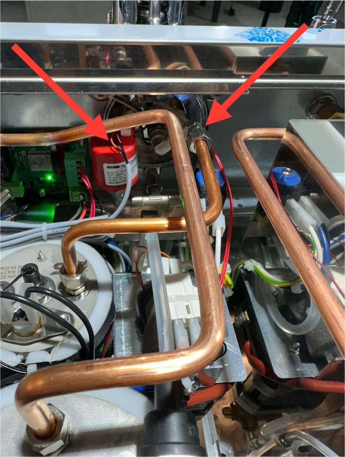Close-up view of the ACS Vostoks's internal components, showing copper pipes and wires. Two red arrows point to specific connection points on the pipes, highlighting areas of interest for repair or inspection.