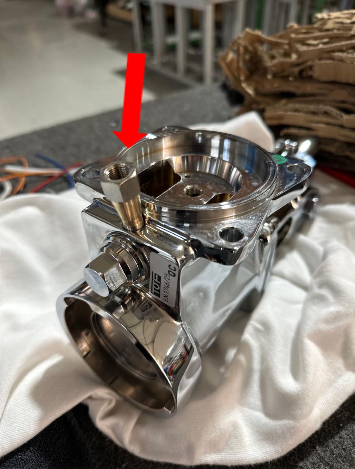 A close-up of the ACS Vostok's grouphead assembly, with a red arrow pointing to a brass fitting attached to the top of the component.