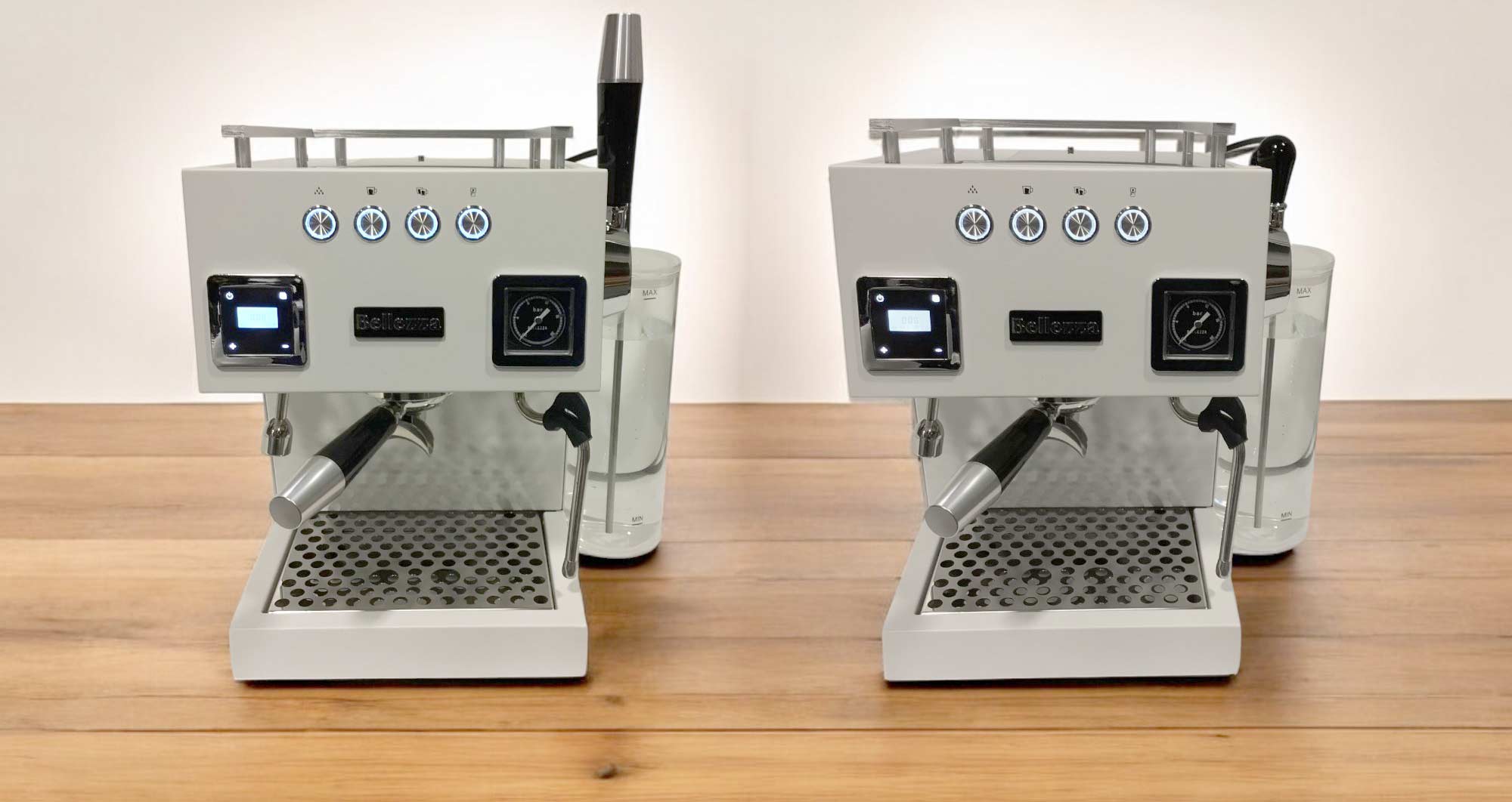 Two identical Bellezza Bellona espresso machines are placed side by side on a wooden surface, each coffee maker featuring buttons, a steam wand, and a drip tray facing forward against a plain white background. © 2025 1st-line.com