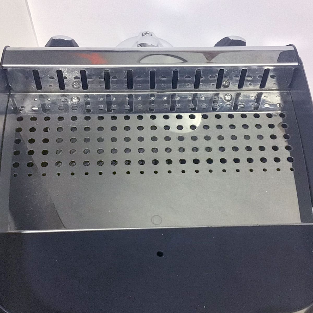 A close-up of a black and silver drip tray with a perforated metal grate and slotted metal back, part of the used SIDEWALK SALE - VBM Super Digital DUAL PROFILER Dual Boiler Espresso Machine (E111), set against a white background. © 2025 1st-line.com