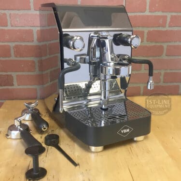 A SIDEWALK SALE - VBM Super Digital DUAL PROFILER Dual Boiler Espresso Machine (used) (E111) sits on a wooden table, surrounded by coffee accessories—ready for your Sidewalk Sale pickup. © 2025 1st-line.com