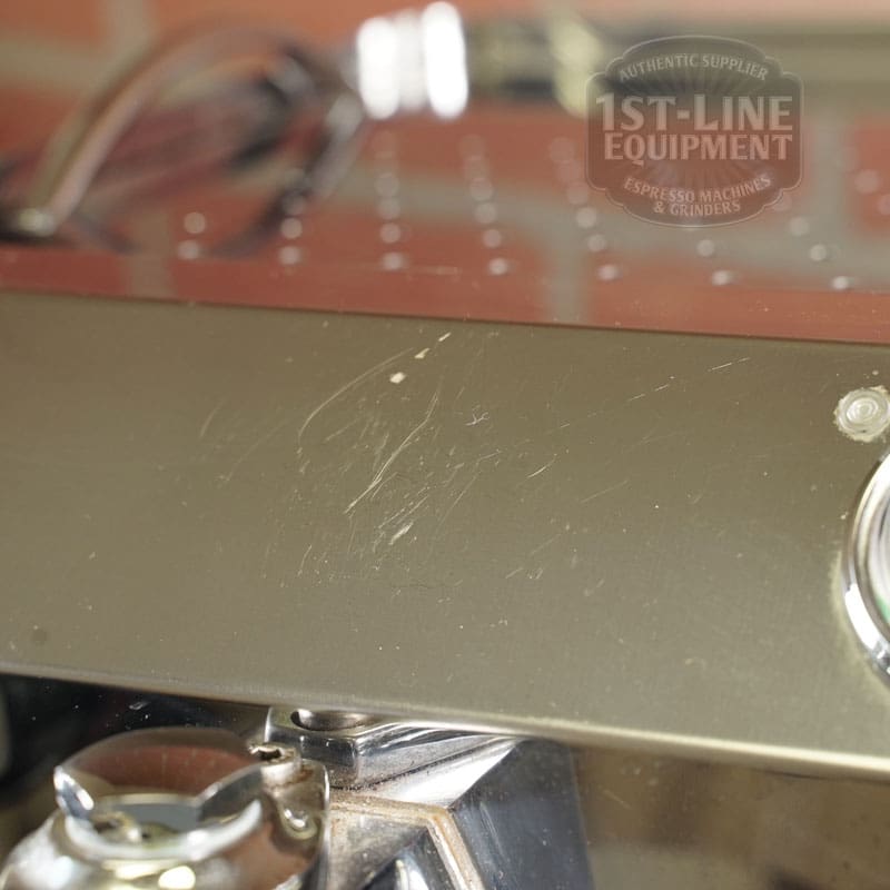 Close-up of a scratched stainless steel surface; the blurred “1st-Line Equipment” logo is in the background. A portion of the SIDEWALK SALE - VBM Domobar Super HX Tank Espresso Machine (USED) (E111) appears at the bottom, ideal for display. © 2025 1st-line.com