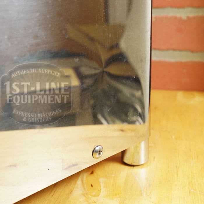 Close-up of the SIDEWALK SALE - VBM Domobar Super HX Tank Espresso Machine (USED) (E111) with 1st-Line Equipment logo reflected on its surface, resting on a wooden counter beside a brick wall—ideal for your next sidewalk sale. © 2025 1st-line.com