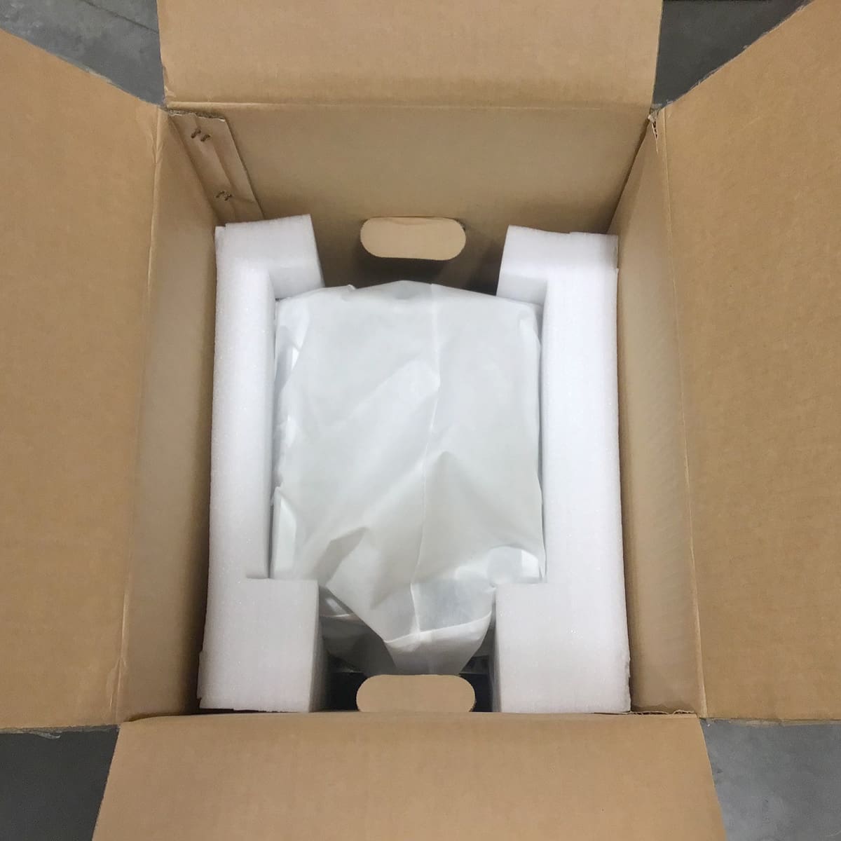 A Bellona cardboard box opened from the top, showing an item wrapped in white paper and secured with white foam padding at the corners for safe packing during shipping. © 2025 1st-line.com