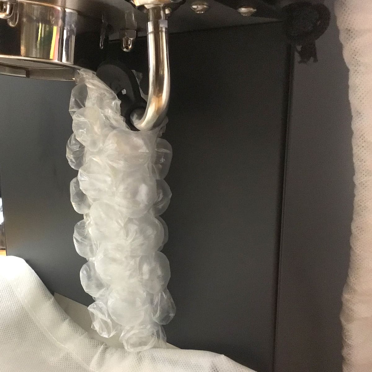 A clear plastic packing glove is stuck under the metal steam wand of a Bellezza Bellona espresso machine, with the fingers twisted and inflated as steam is emitted. © 2025 1st-line.com