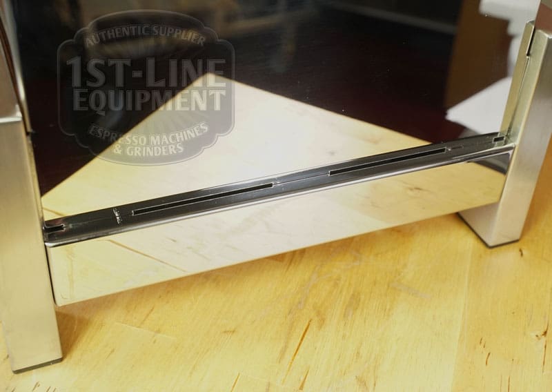 A close-up of a glass panel with two metal brackets on wood, faintly reflecting the LIKE NEW - Elektra Verve Dual Boiler Espresso Machine (C104) and 1st-Line Equipment logo in the background—looks like new. © 2025 1st-line.com