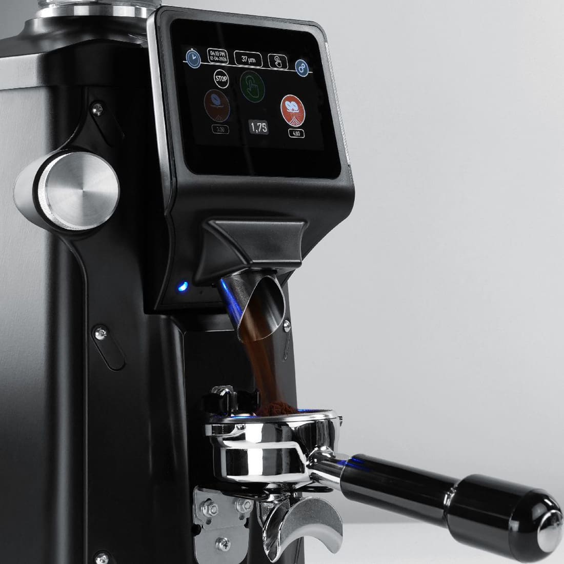 A close-up of the Quamar Alpha 65 Q Espresso Coffee Grinder, featuring a digital touchscreen interface, dispensing ground coffee into a portafilter positioned beneath its spout. © 2025 1st-line.com