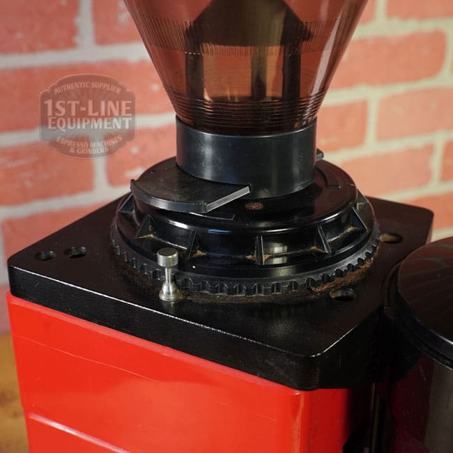 A close-up of the SIDEWALK SALE - Cunill Doser Grinder (E012) shows its adjustment dial on a red base, black plastic hopper, and grind size indicator. The 1st-Line Equipment logo appears on a brick wall in the background. © 2025 1st-line.com