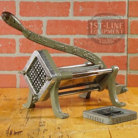 A SIDEWALK SALE - Halco French Fry Cutter Maker (E110) with lever and grid blades rests on a countertop before a brick wall, with an extra blade grid placed nearby. © 2025 1st-line.com