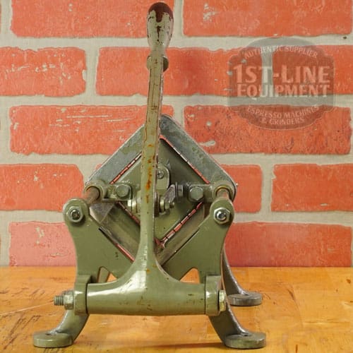 A vintage Halco French Fry Cutter Maker (E110) from SIDEWALK SALE, finished in green, stands with its lever upright on a wooden surface before a red brick wall—its sturdy build reflecting an industrial design ideal for collectors. © 2025 1st-line.com