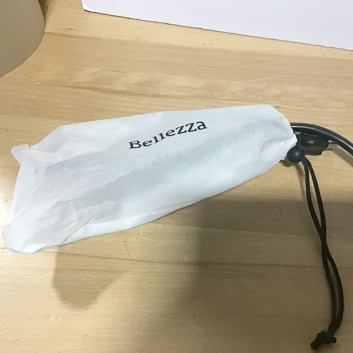 A white mesh drawstring packing bag with the word Bellezza printed on it lies on a light wooden surface. © 2025 1st-line.com