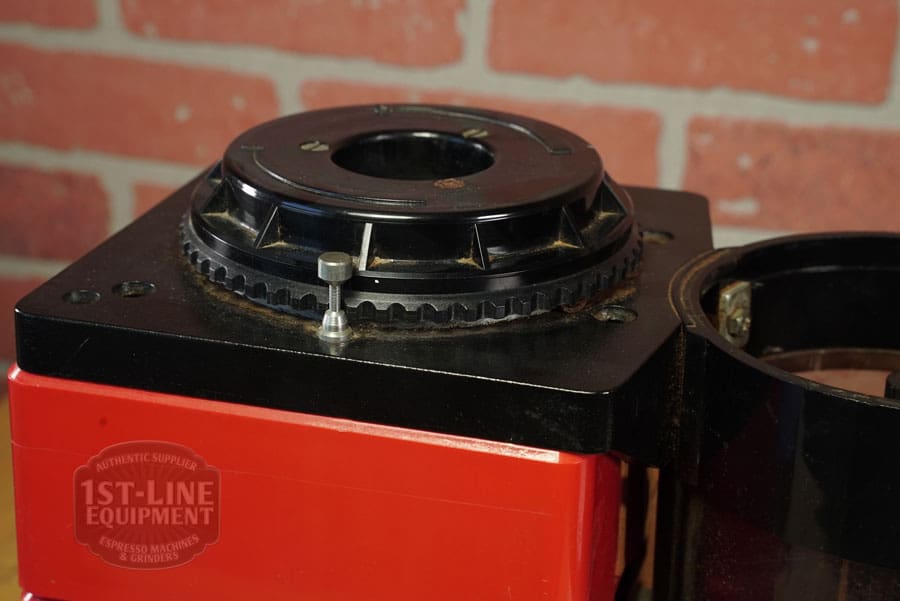 Close-up of the SIDEWALK SALE - Cunill Doser Grinder (E012) in red, featuring a black adjustment ring and silver screw, with the 1st-Line Equipment logo visible—ideal for your next sidewalk sale display against a brick wall backdrop. © 2025 1st-line.com