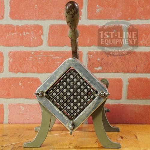 The SIDEWALK SALE - Halco French Fry Cutter Maker (E110) features a grid of blades and handle, displayed on wood against a brick wall—an eye-catching addition to your next sidewalk sale. © 2025 1st-line.com