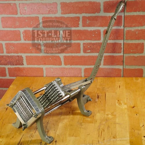 The SIDEWALK SALE - Halco French Fry Cutter Maker (E110) features a vintage lever-operated grid blade, displayed on a wooden surface against a red brick wall—an ideal addition to your next sidewalk sale find. © 2025 1st-line.com
