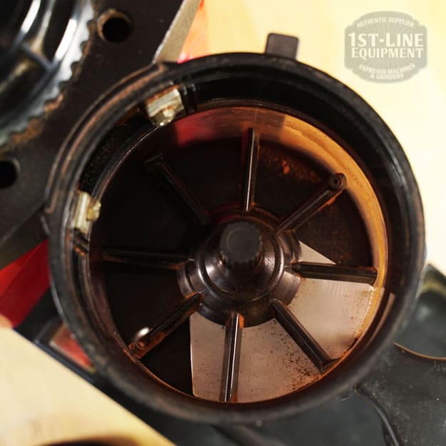 Top-down view of the SIDEWALK SALE - Cunill Doser Grinder (E012) interior, featuring metal blades and some leftover coffee grounds. The 1st-Line Equipment logo appears in the upper right corner, marking this special find. © 2025 1st-line.com