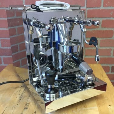 A SIDEWALK SALE - Bellezza Inizio R Leva HX Espresso Machine (USED)(E314) with multiple knobs, levers, and a pressure gauge sits on a wooden countertop. Accessories like a tamper and portafilter rest on the drip tray. © 2025 1st-line.com