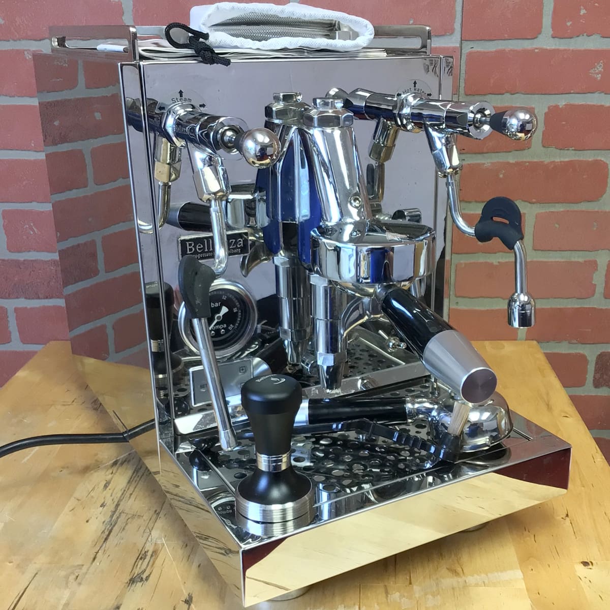 A SIDEWALK SALE - Bellezza Inizio R Leva HX Espresso Machine (USED)(E314) with multiple knobs, levers, and a pressure gauge sits on a wooden countertop. Accessories like a tamper and portafilter rest on the drip tray. © 2025 1st-line.com