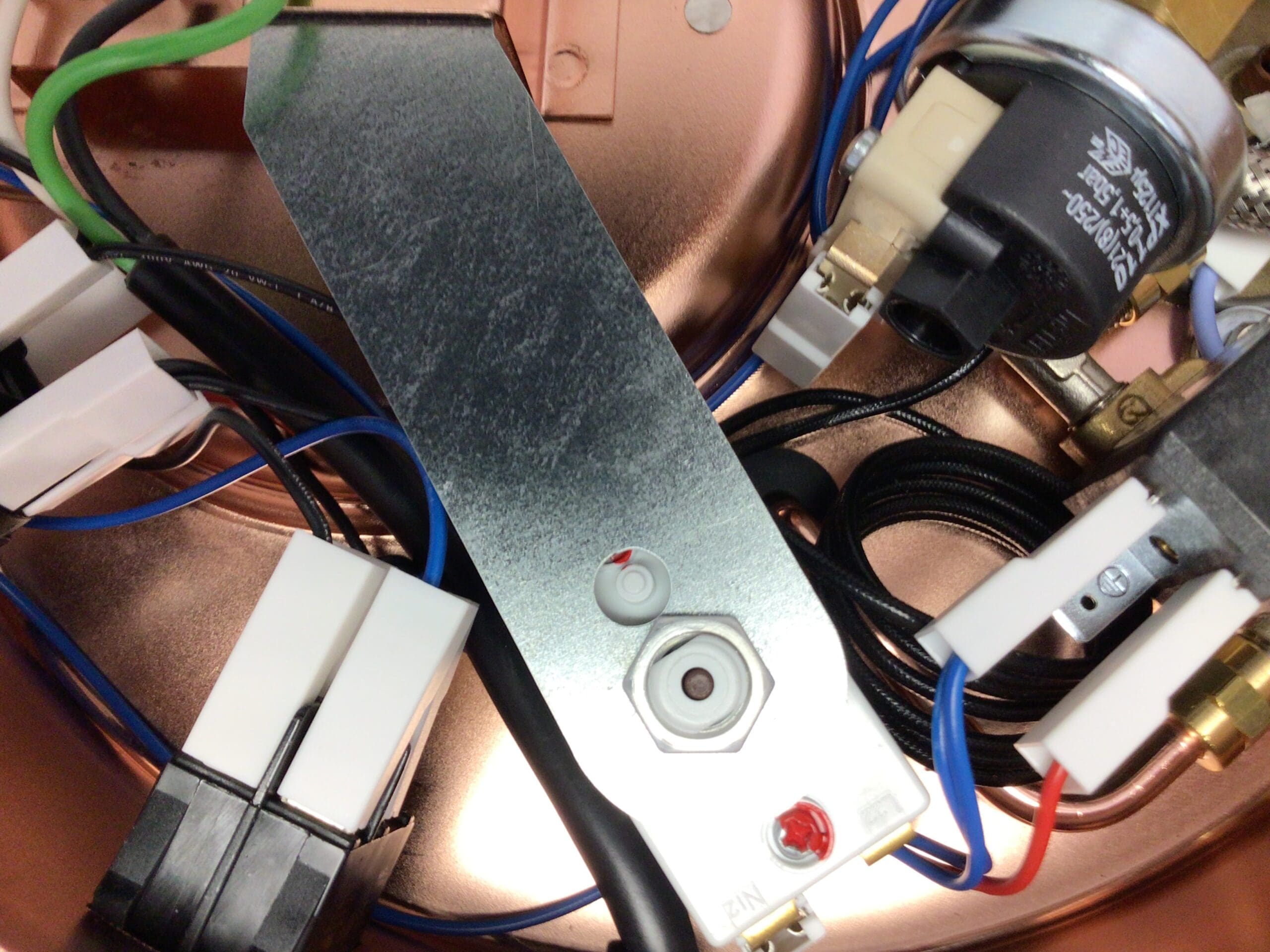 Close-up of electrical components inside an Elektra Semiautomatica device, showing wires, connectors, and a metal plate with labeled buttons and indicator lights. Copper and plastic materials are visible in the background. &copy; 2025 1st-line.com