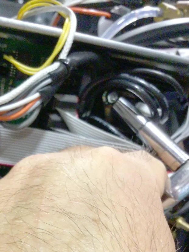 A close-up of a hand using a socket wrench to tighten or loosen a bolt among various cables and wires inside a Carimali Bubble, possibly while performing a Swap Triac repair. © 2025 1st-line.com
