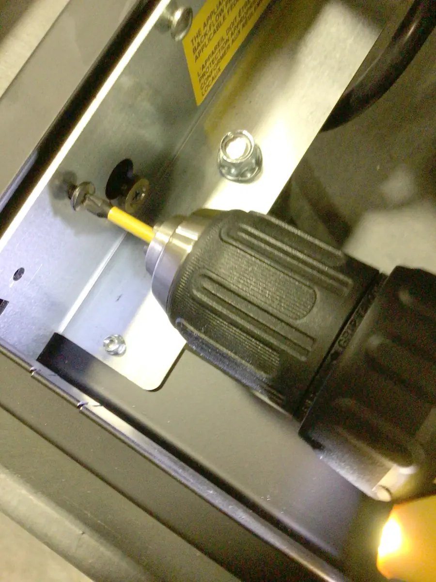 A close-up of a power drill with a yellow bit fastening a screw into a metal panel on a Carimali Bubble machine. The drill is angled, and part of the mechanical assembly, including the Swap Triac area, is visible in the background. © 2025 1st-line.com
