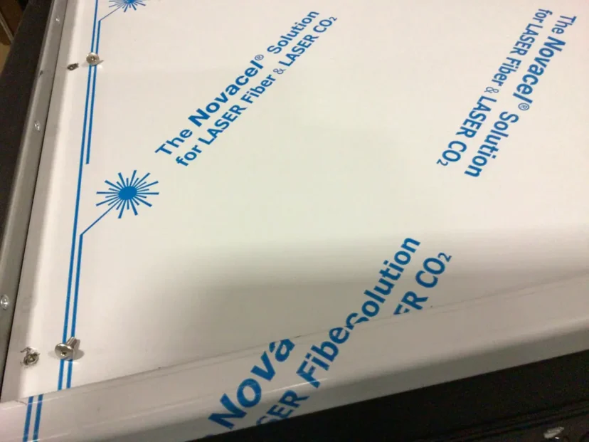 A close-up of a white panel with blue text that reads “The Novace Solution for LASER Fiber & LASER CO2,” alongside a Swap Triac detail, featuring a blue laser graphic and several screws securing the panel. © 2025 1st-line.com