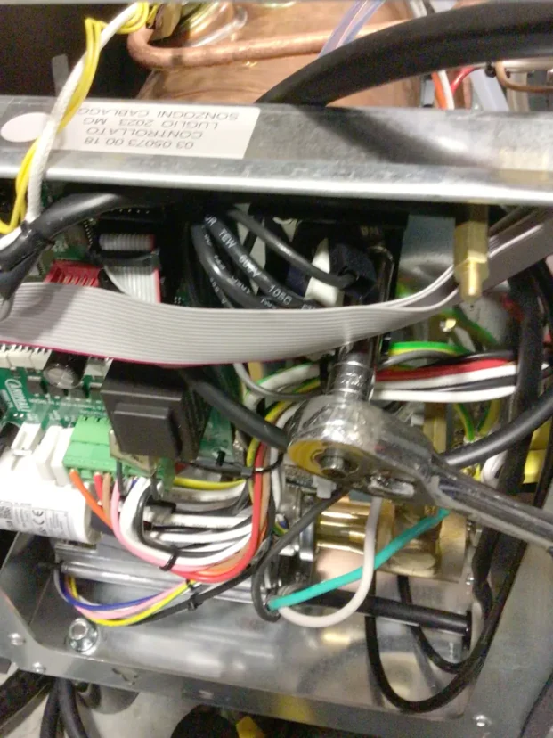 A close-up view of the inside of an electronic device, showing various colored wires, circuit boards, and a wrench tightening a bolt on a metallic component. © 2025 1st-line.com