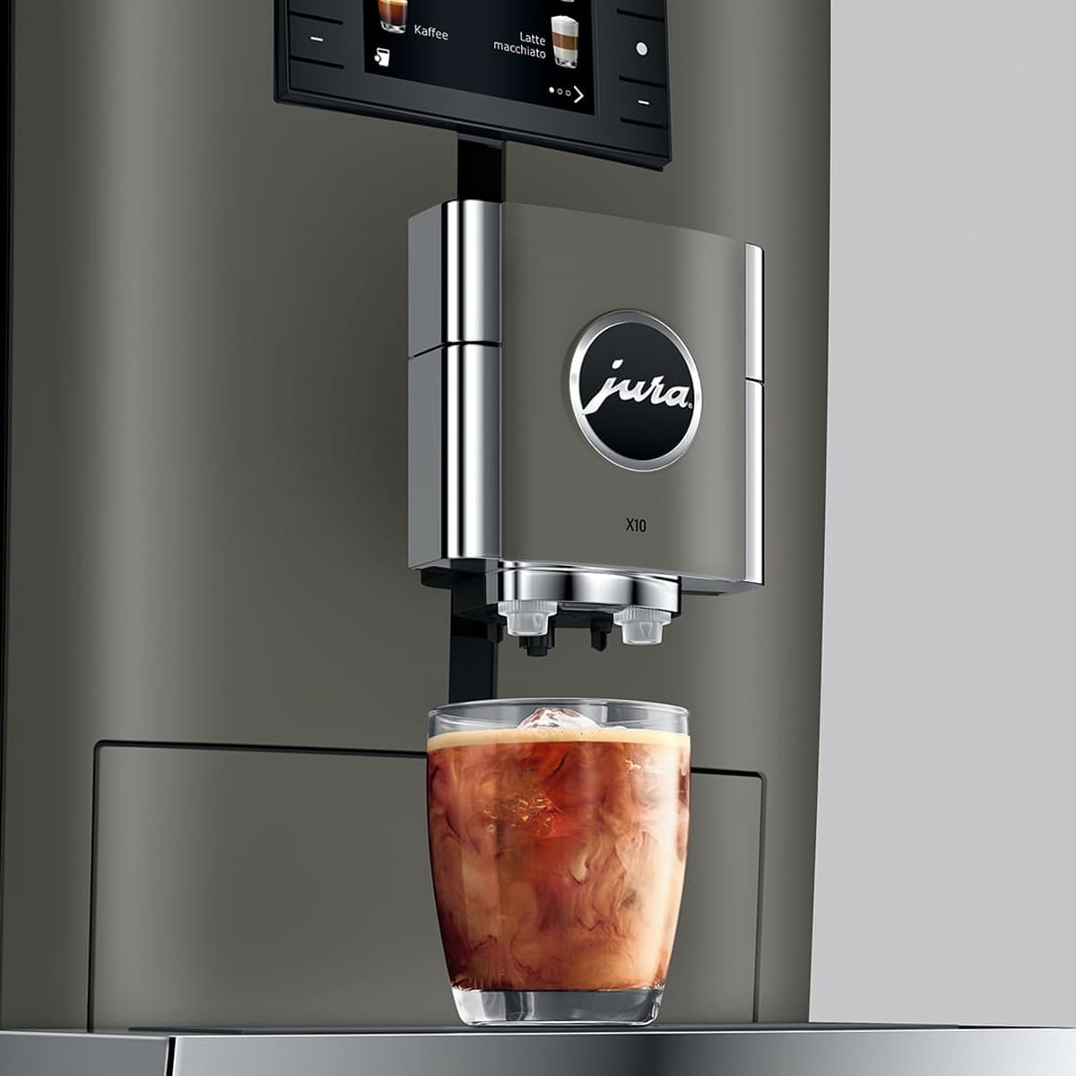 A glass of iced coffee with swirling milk rests beneath the Jura X10 Super-Automatic Espresso Machine, showcasing its sleek metallic design and modern digital display. © 2025 1st-line.com