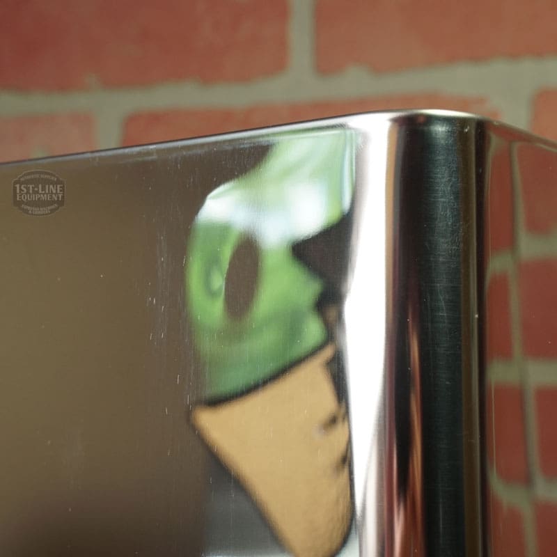 A green toy or figurine holding a brown cone is reflected on the shiny metal surface of a Lelit 1400160 Back Body Panel (with dents), set against a brick wall background. © 2025 1st-line.com
