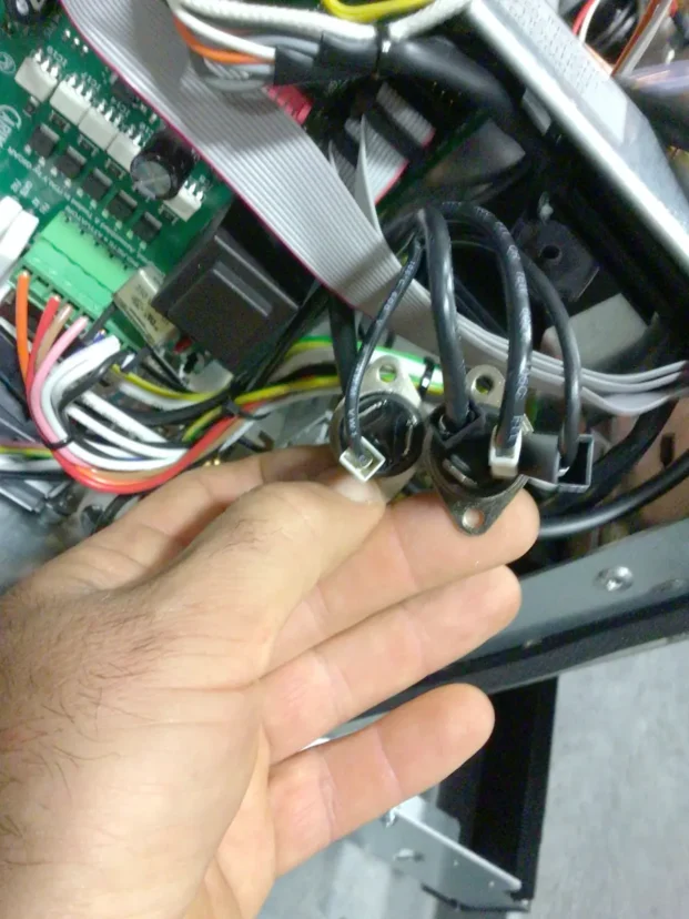 A hand holding two black wires connected to metal terminals inside a Carimali Bubble machine, with various colored wires, circuit boards, and a Swap Triac visible in the background. © 2025 1st-line.com