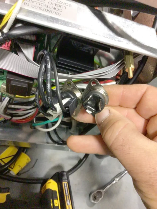 A hand holds two metal temperature sensors with black wires, in front of an open Carimali Bubble electronics panel with various cables, circuits, and tools visible—ideal for a Swap Triac repair or upgrade. © 2025 1st-line.com