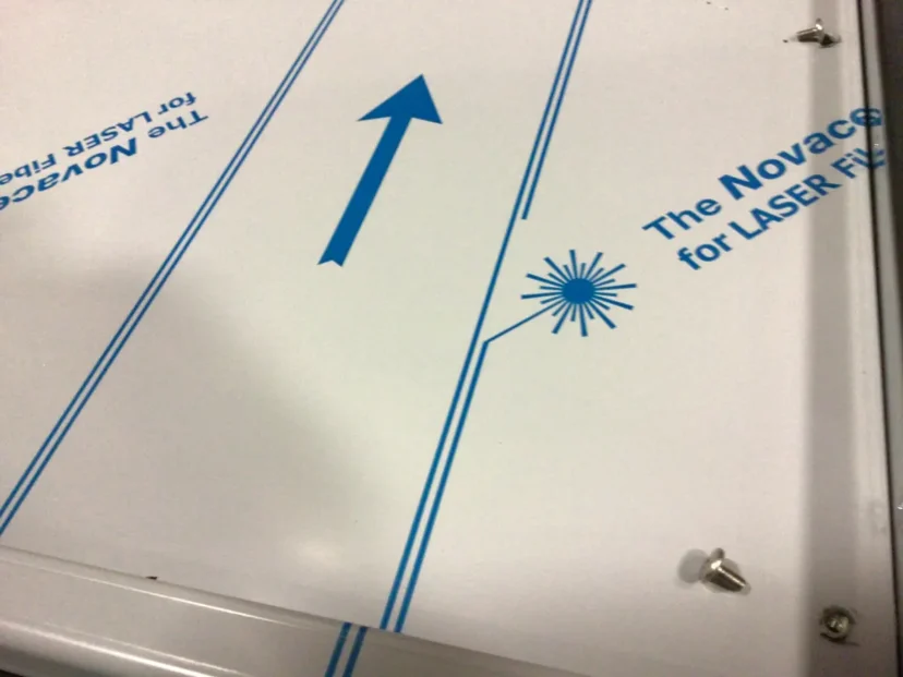 A white surface with blue lines, a large blue arrow, and text reading The Novace for LASER FI. A starburst laser icon and a couple of loose screws share the scene, reminiscent of Carimali Bubble styling. © 2025 1st-line.com
